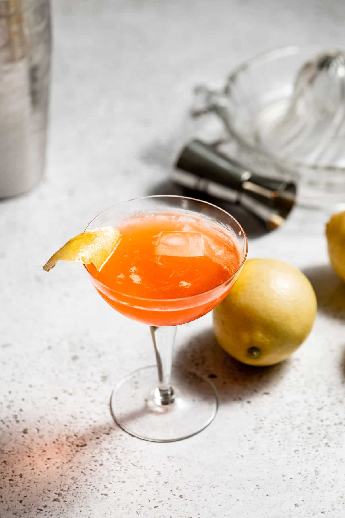 A paper plane cocktail garnished with a lemon twist sitting on a concrete counter.