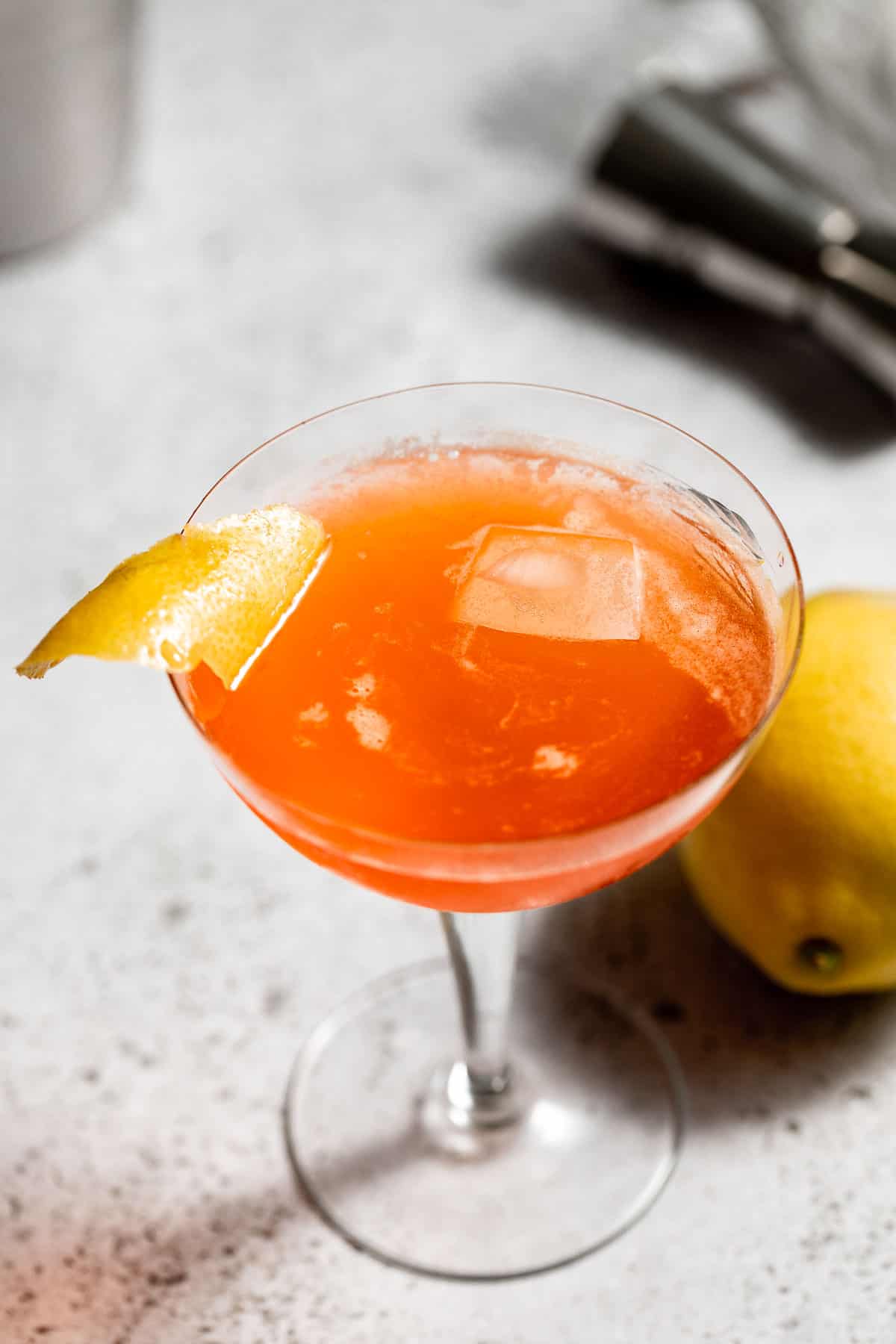 A paper plane cocktail served in a coupe glass and garnished with a lemon twist.