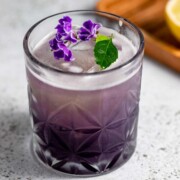 A purple rain cocktail topped with fresh purple flowers.