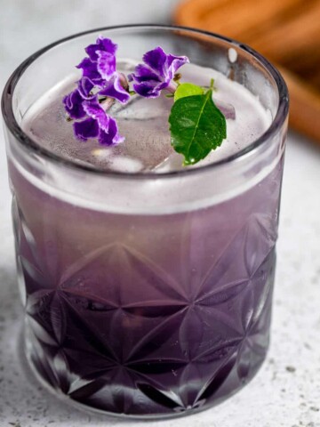 A purple rain cocktail topped with fresh purple flowers.