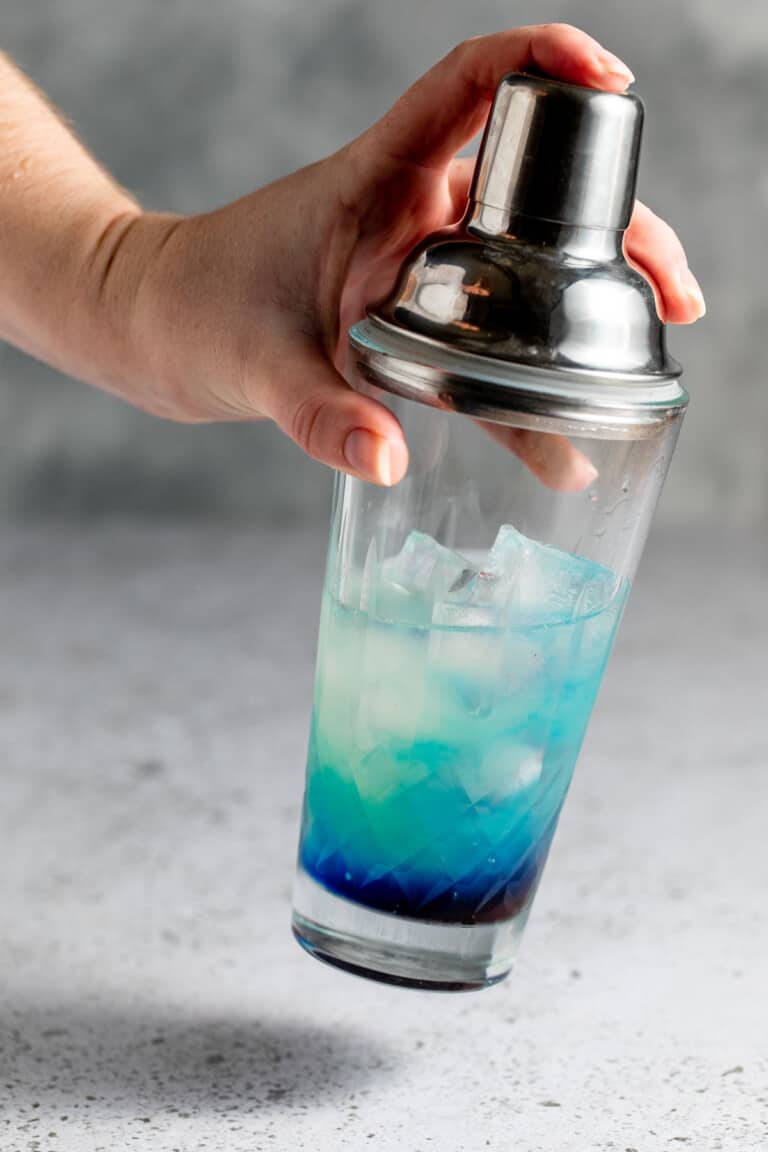 Blue Curacao, grenadine, lime juice and vodka being shaken with ice in a cocktail shaker.