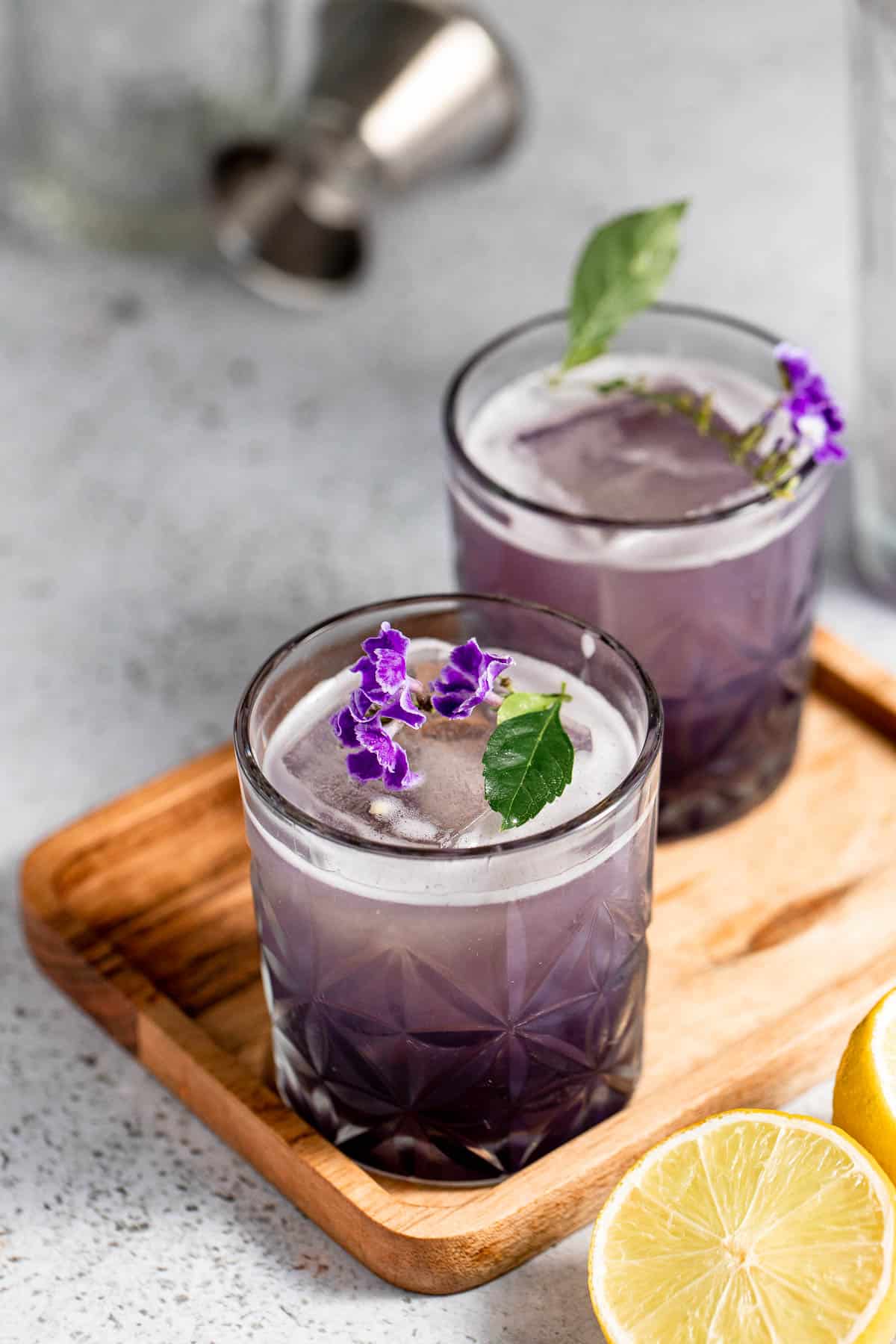 Two glasses of purple rain cocktail topped with fresh flowers.