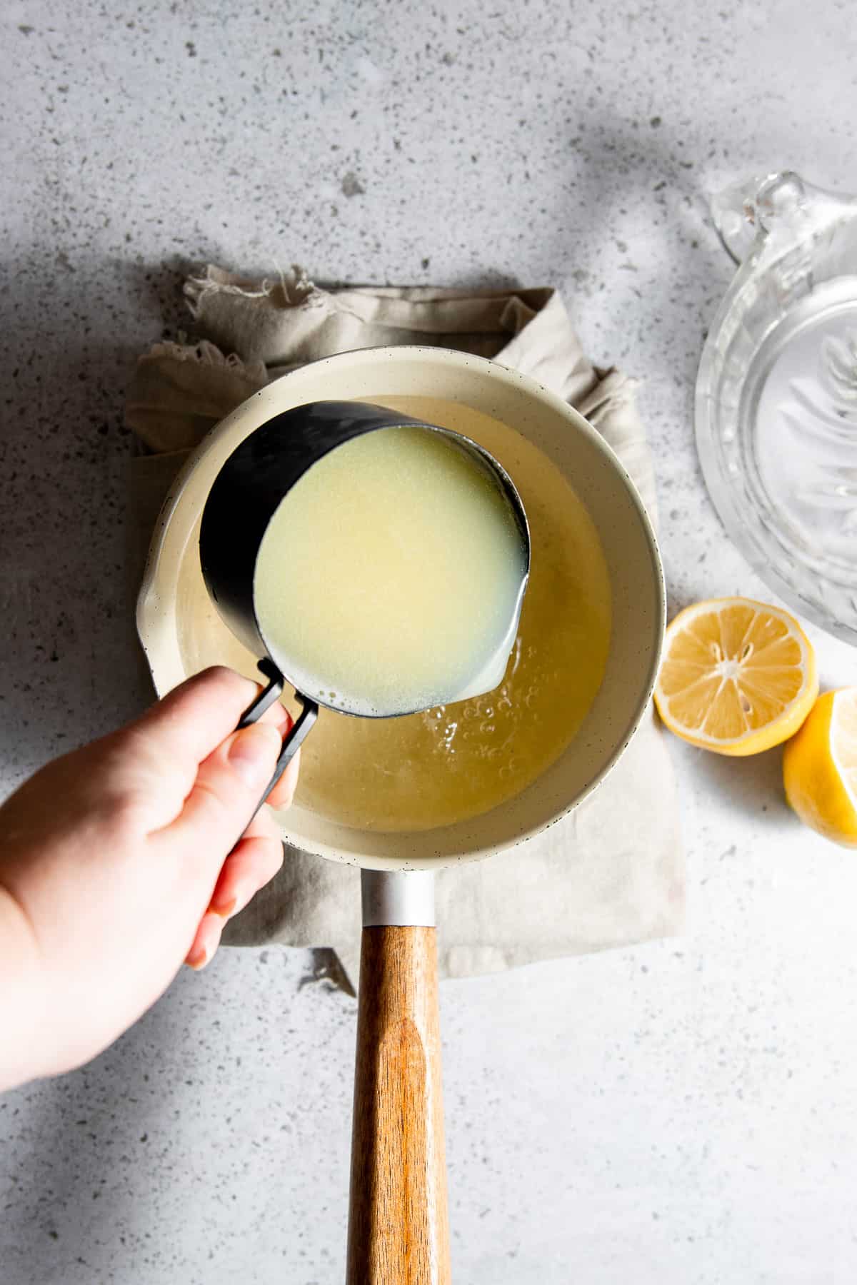 Lemon and lime juice being added to the simple syrup mixture in the saucepan.