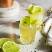 Two shot glasses filled with green tea shot and topped with slices of lime.
