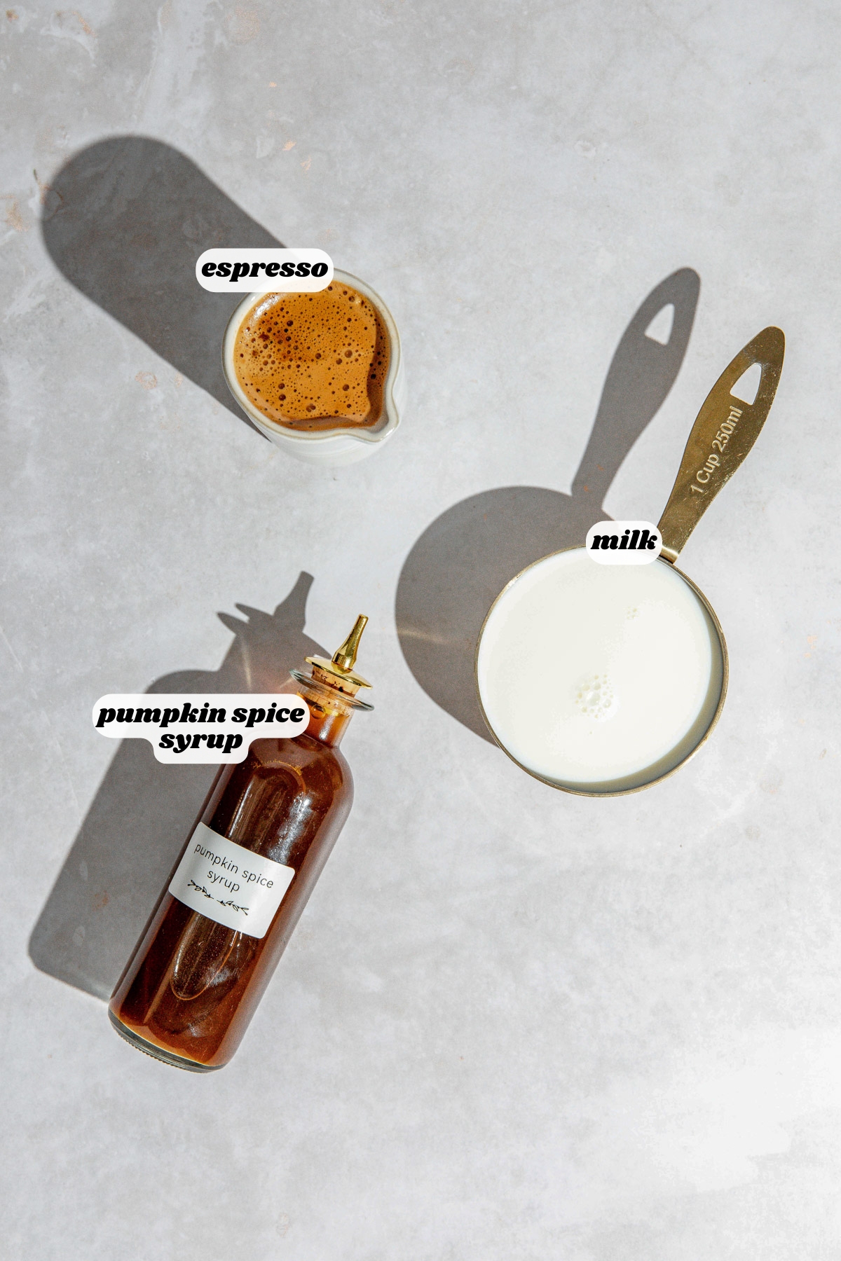 Ingredients for a pumpkin spice latte sitting on a concrete countertop.