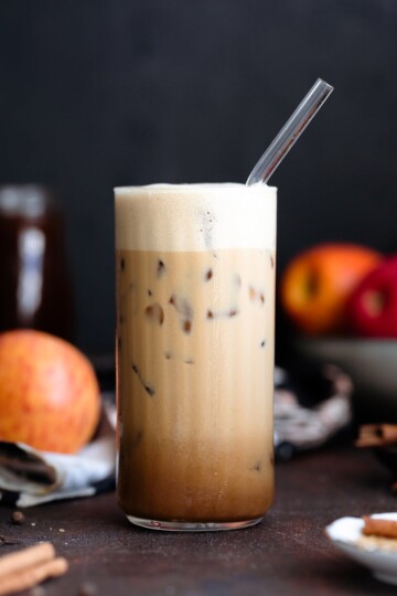 An iced apple crisp macchiato served in a tall glass with a straw.