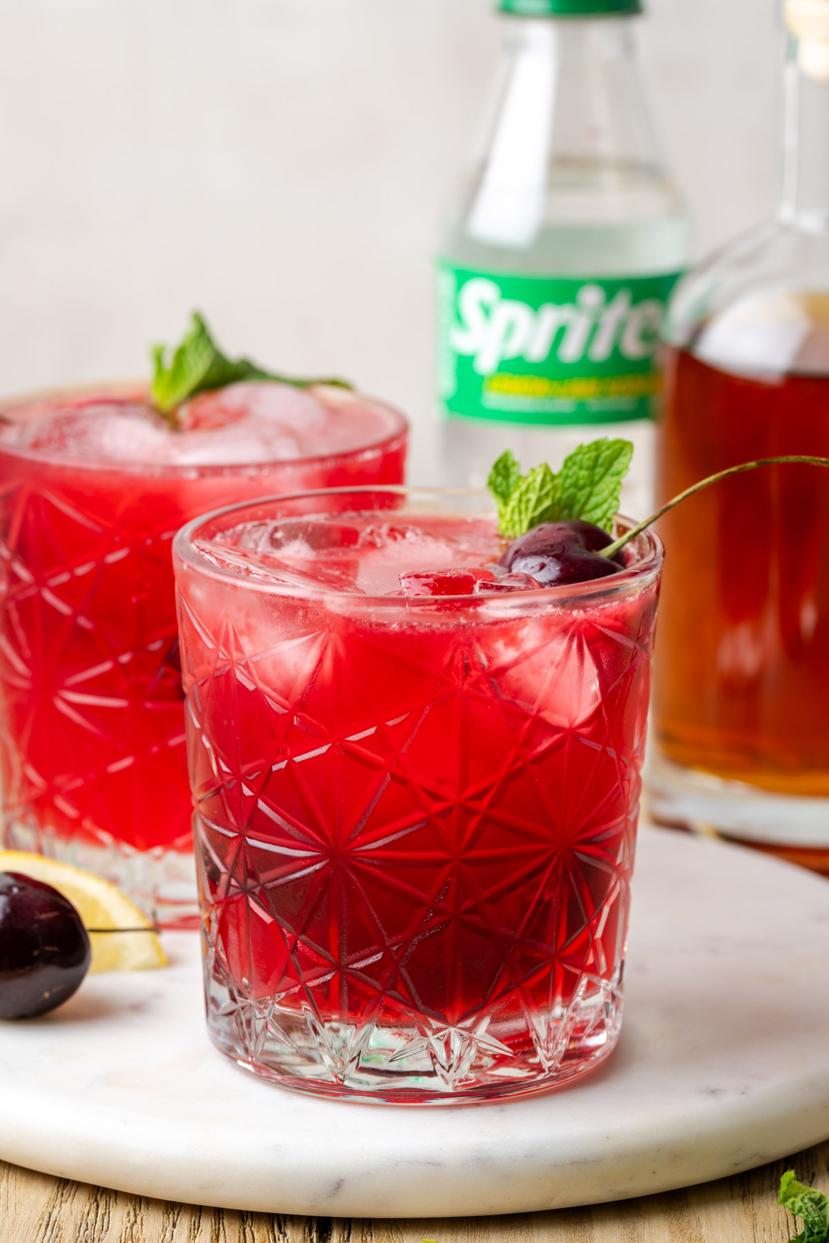 Two rocks glasses filled with cherry bourbon smash sitting on a marble tray.