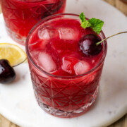 A cherry bourbon smash served in a rock glass and garnished with fresh cherries and mint leaves.