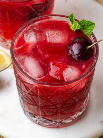 A cherry bourbon smash served in a rock glass and garnished with fresh cherries and mint leaves.