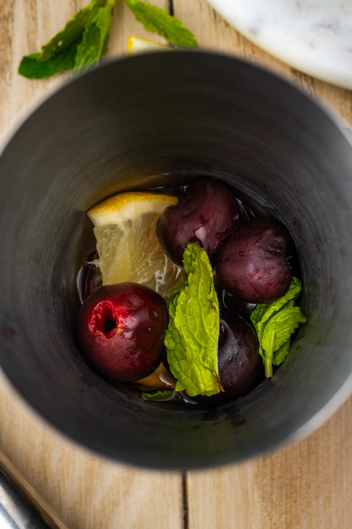 Cherries, lemon wedges, mint leaves and bourbon in a cocktail shaker.