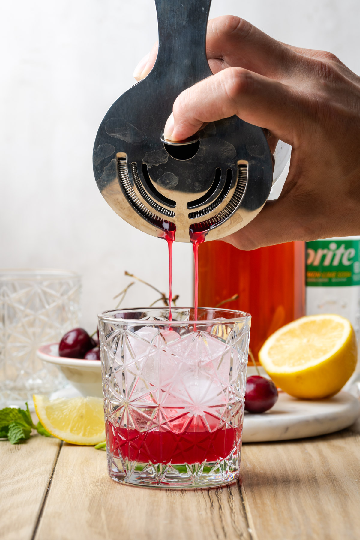 A cherry bourbon smash being poured through a strainer into a rocks glass.