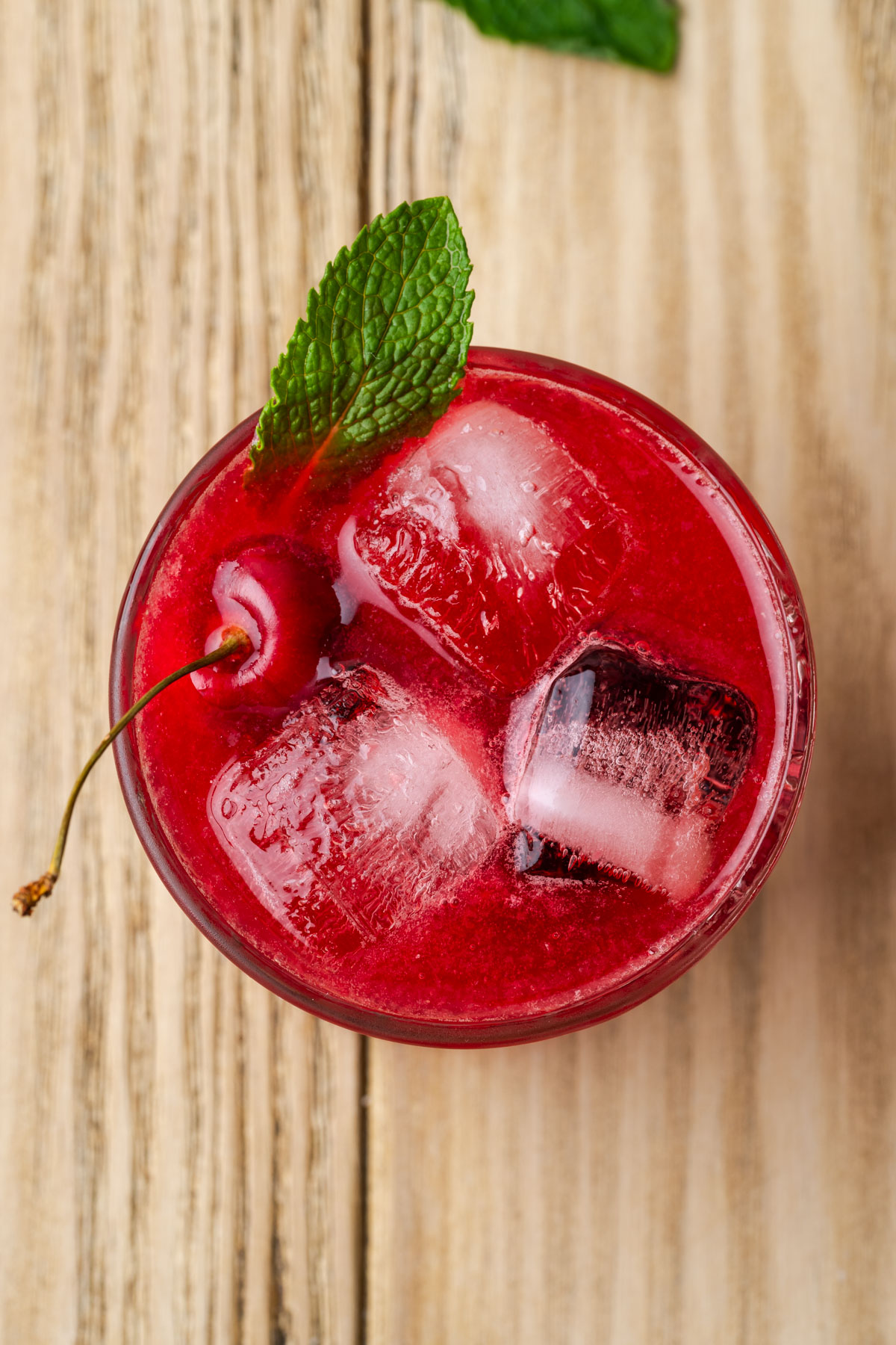 A rocks glass filled with cherry bourbon smash cocktail.