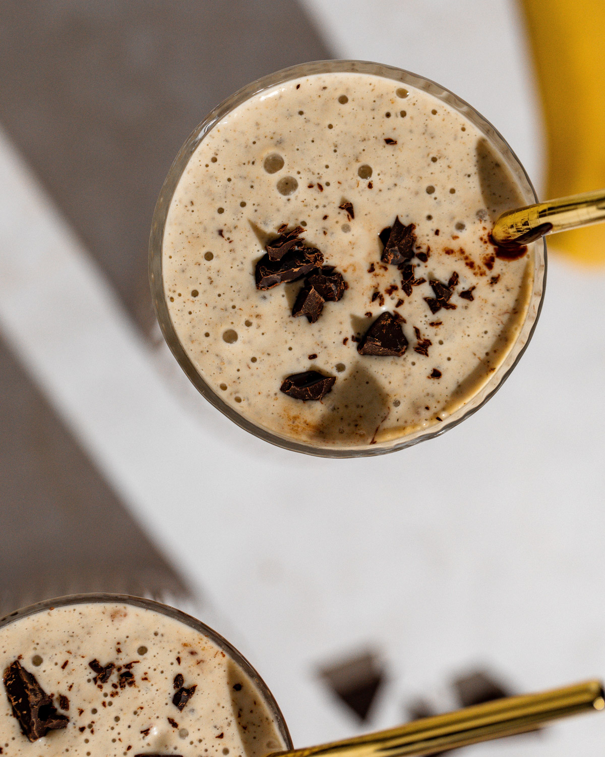 Two glasses of chocolate peanut butter smoothie sitting on a white table.