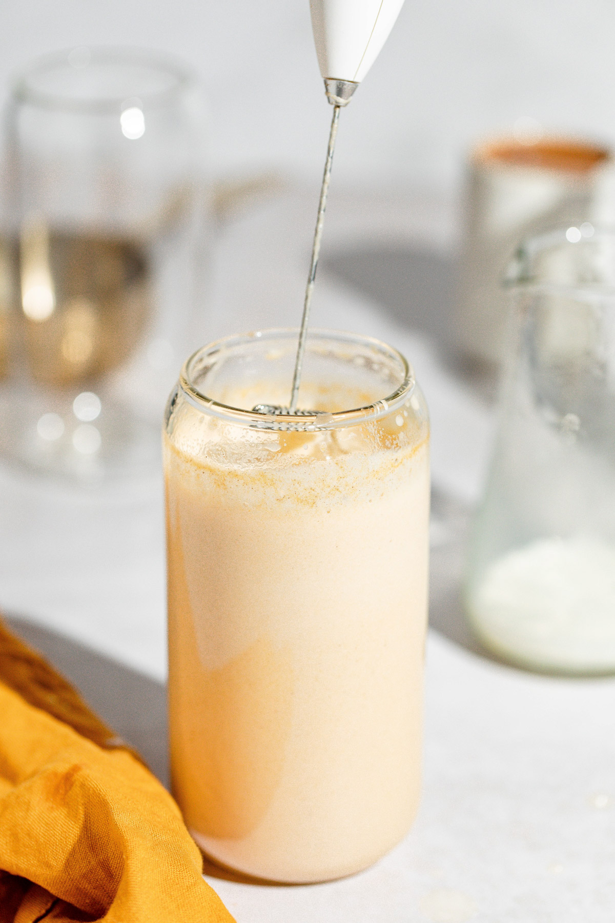 Pumpkin spice syrup and milk being mixed together with a milk frother in a tall glass.