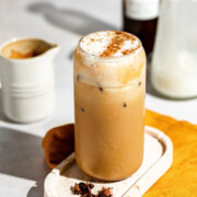 A tall glass filled with an iced pumpkin spice latte topped with cinnamon.