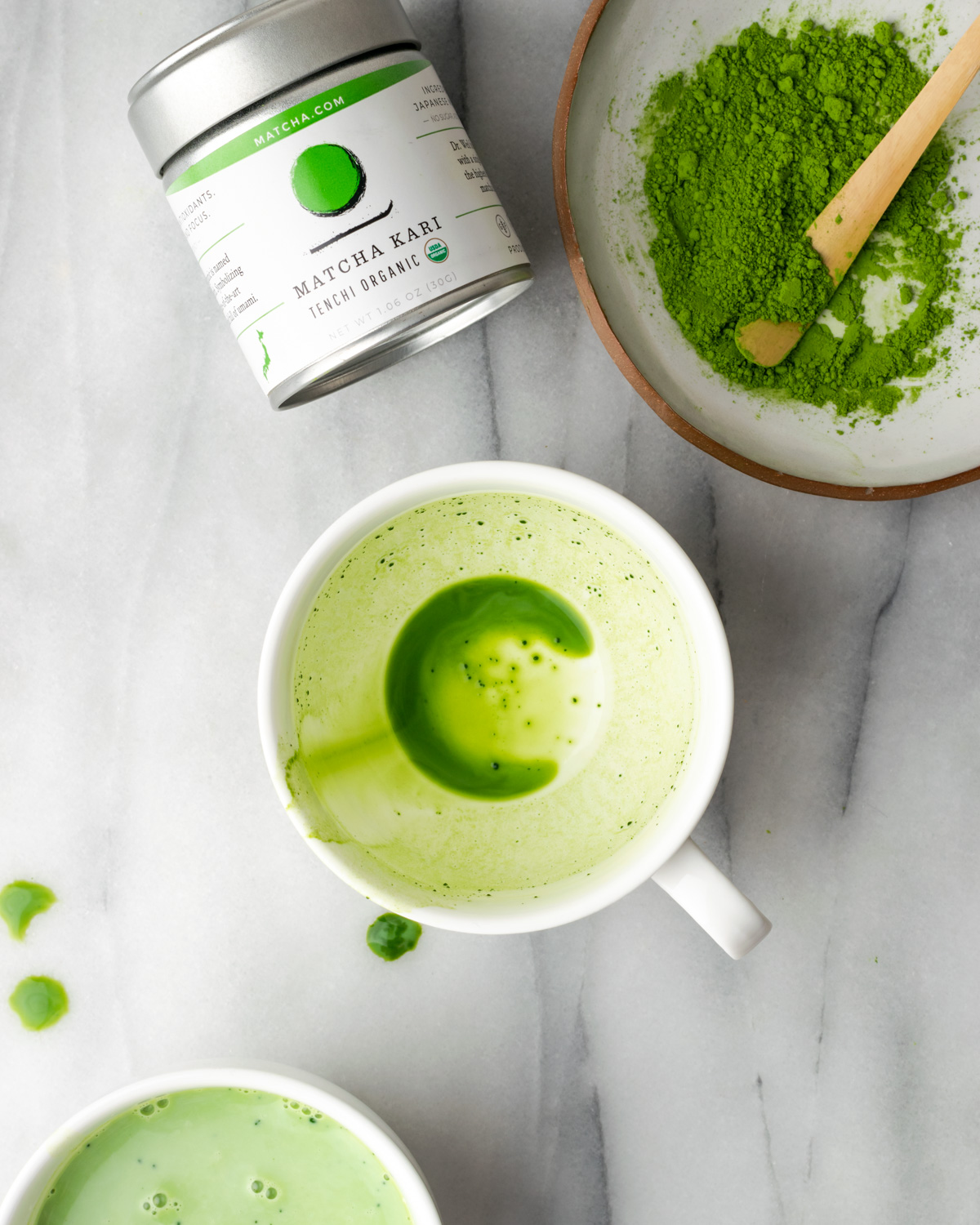 A coffee mug with the remnants of green tea next to a dish of matcha powder.