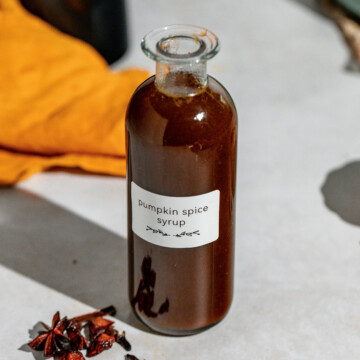 A glass jar of pumpkin spice syrup sitting on a concrete countertop.