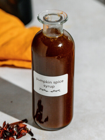 A glass jar of pumpkin spice syrup sitting on a concrete countertop.