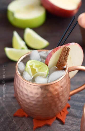 An apple cider Moscow mule garnished with a cinnamon stick and slice of fresh apple.