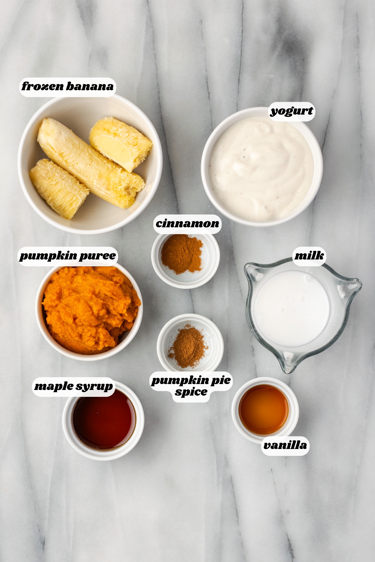 Ingredients for a pumpkin spice smoothie sitting on a marble counter.