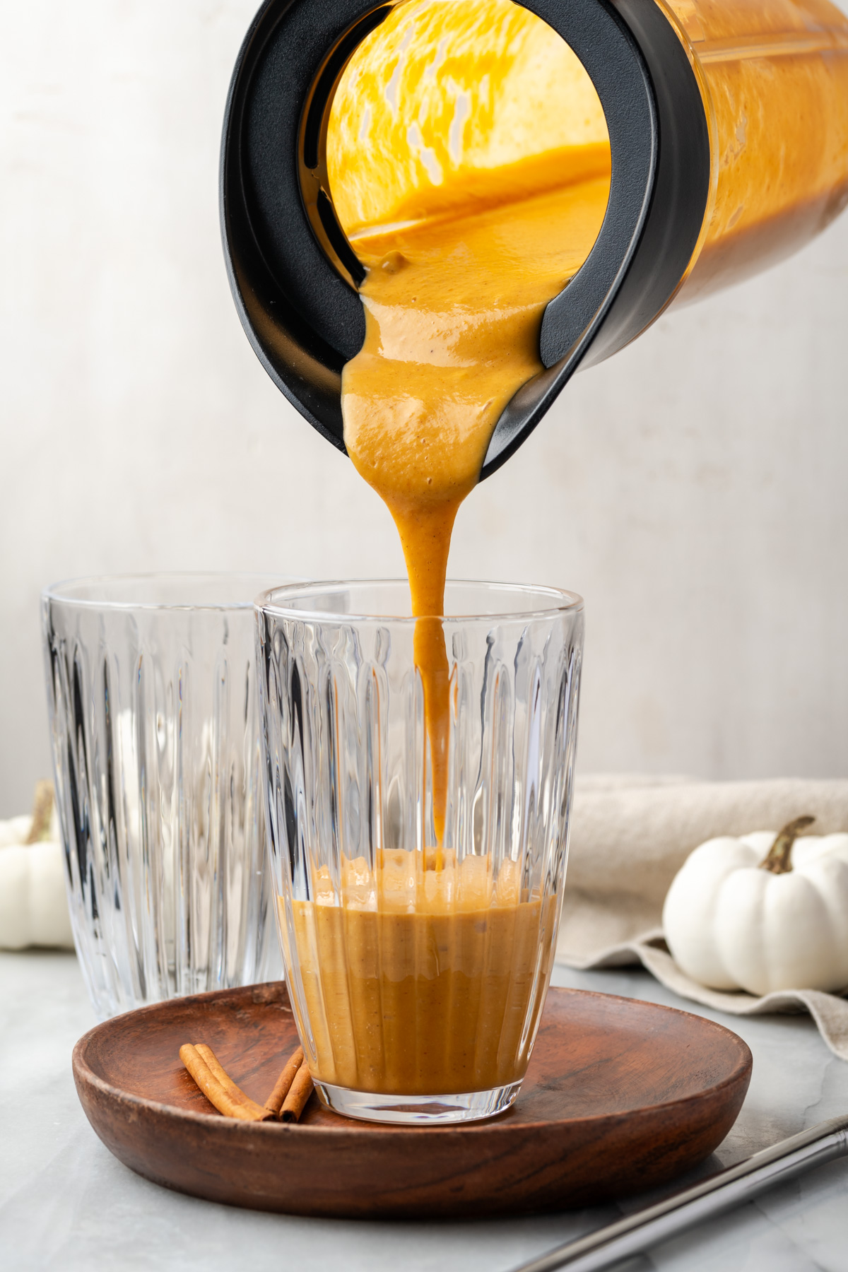 A pumpkin spice smoothie being poured from a blender into a tall glass.