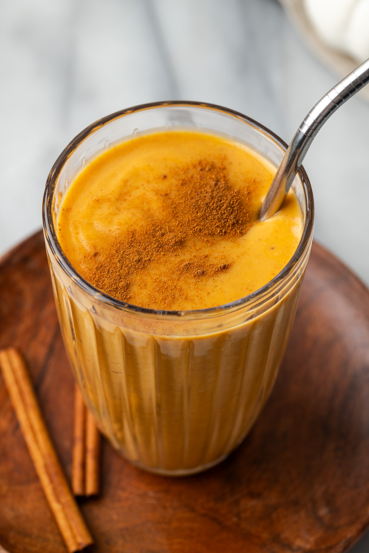 A pumpkin spice smoothie topped with a sprinkle of cinnamon, sitting on on a wood tray.