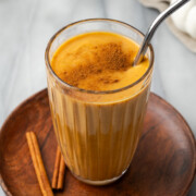 A glass of pumpkin spice smoothie sitting on a wood tray.