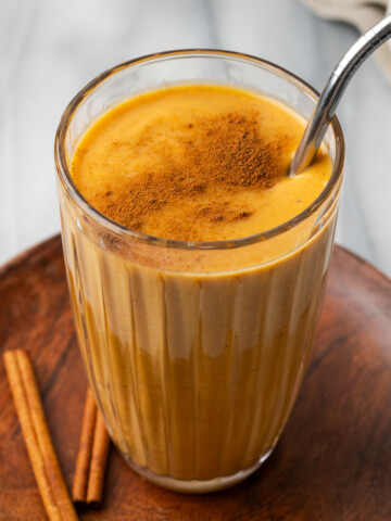 A glass of pumpkin spice smoothie sitting on a wood tray.