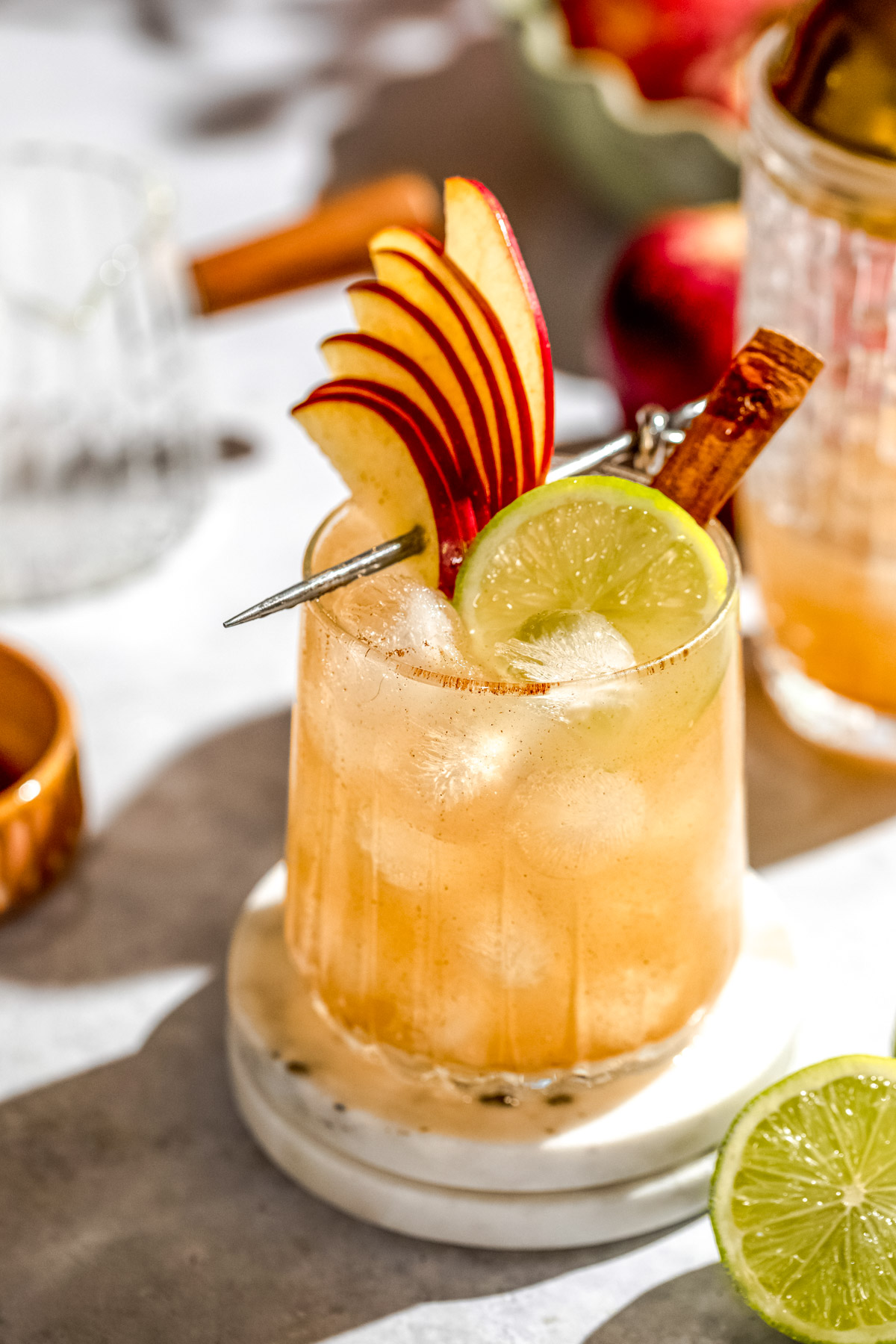 An apple cider margarita garnished with fresh apple slices and lime on a countertop. 