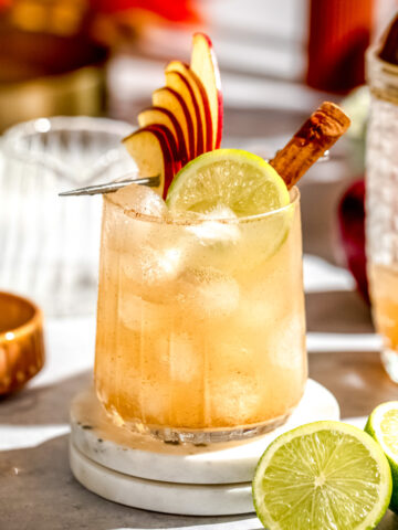 An apple cider margarita garnished with fresh apple slices and a lime wedge.