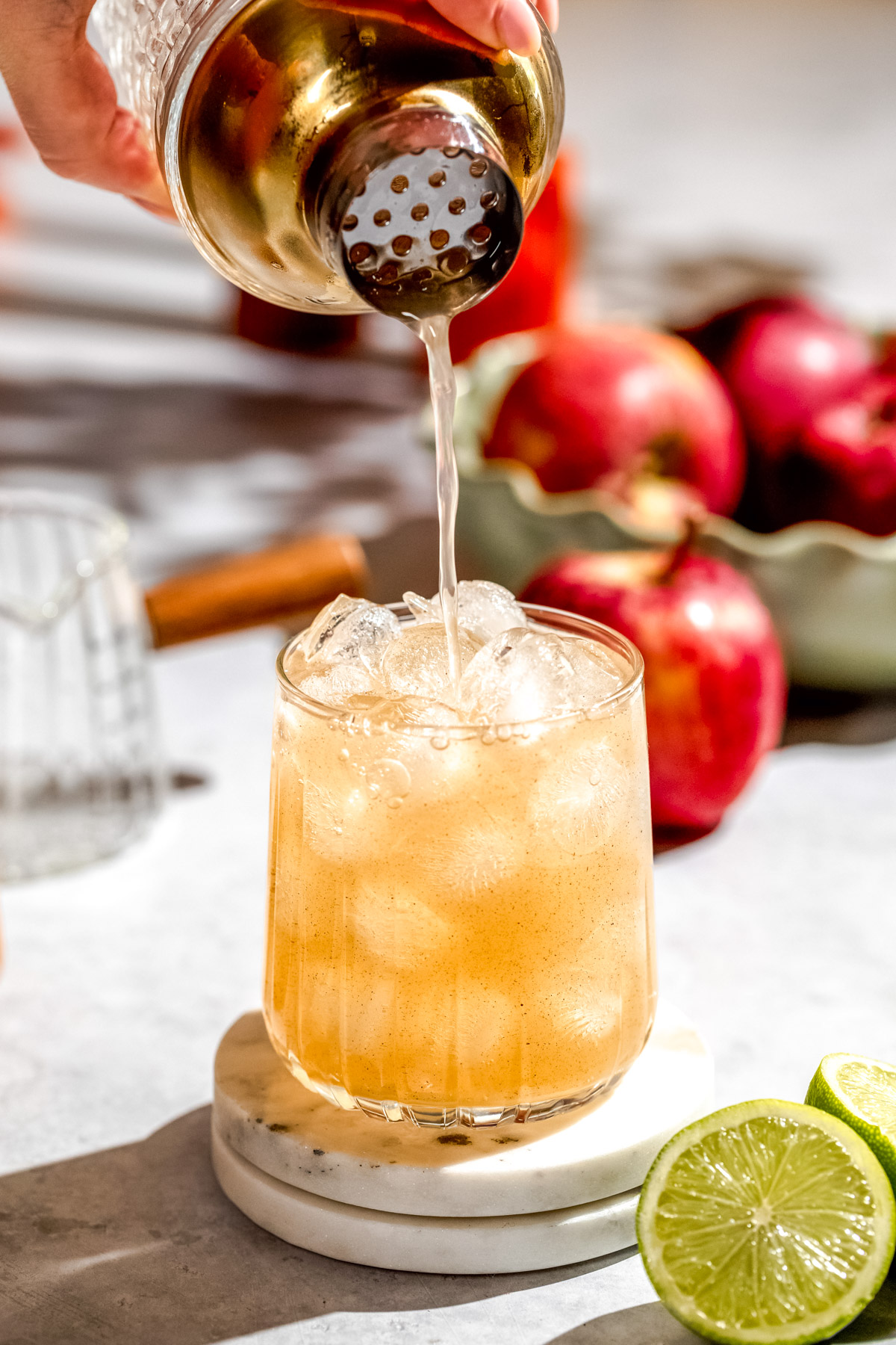 An apple cider margarita being poured into a serving glass from a cocktail shaker.