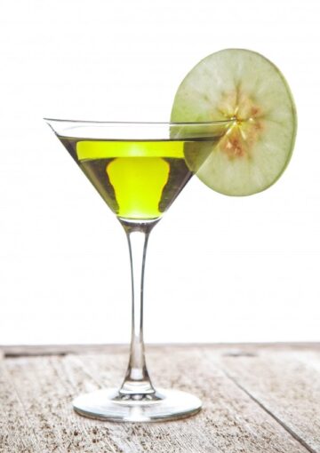 A martini glass filled with a green appletini cocktail and garnished with a slice of fresh apple.